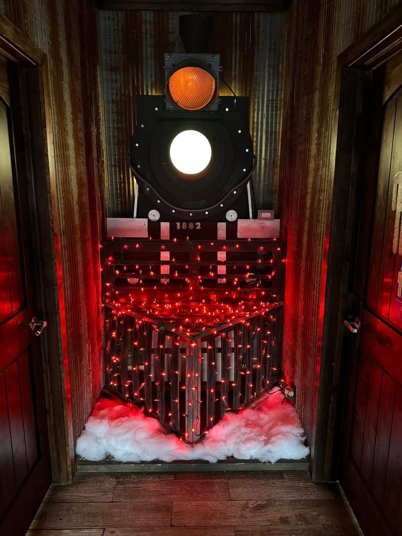 A train engine decoration with red lights and artificial snow, flanked by wooden doors.