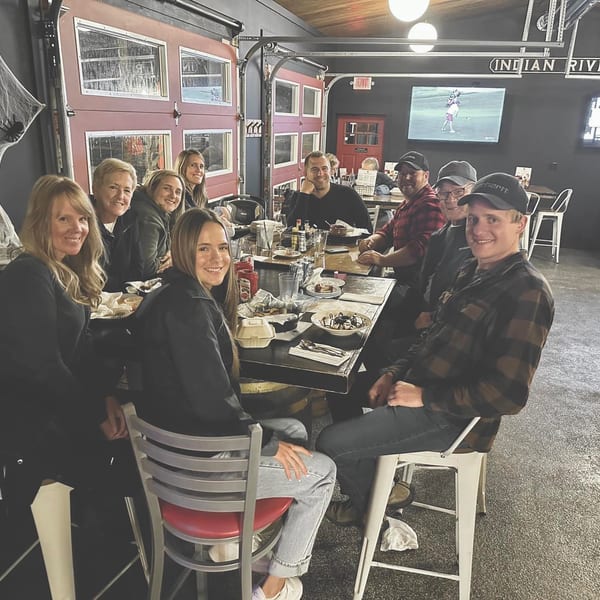 A group of people smiling and dining at a long table in a restaurant with Halloween decorations.