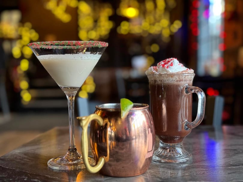 Three festive drinks: a martini, a Moscow mule, and a hot chocolate with whipped cream.
