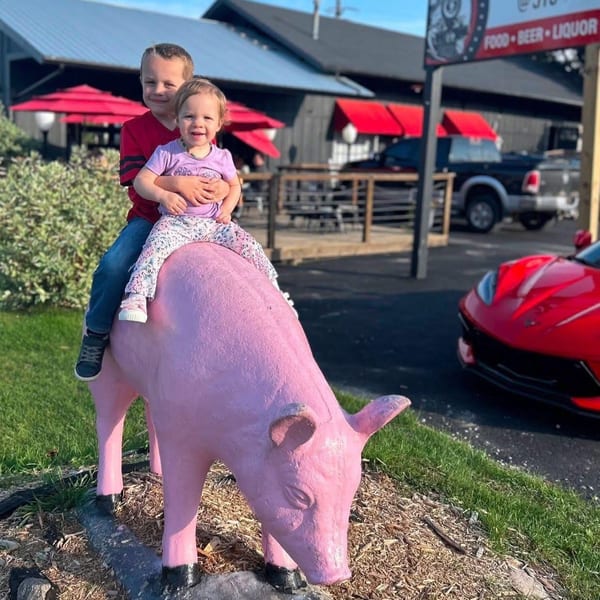 Two young children sit atop a pink pig statue outside The Station @310 restaurant.