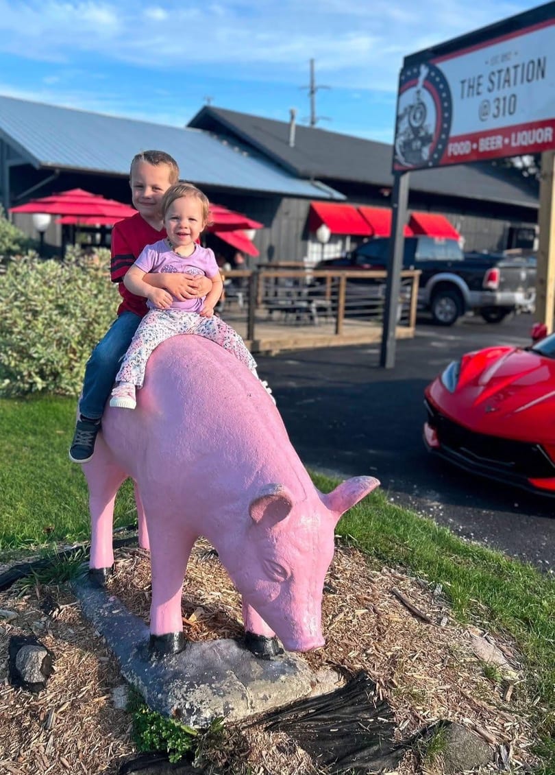 Two young children sit atop a pink pig statue outside The Station @310 restaurant.