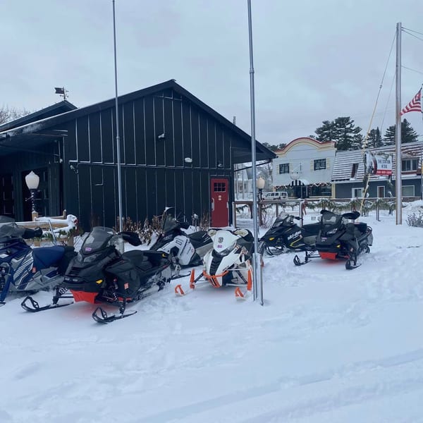 Snowmobiles parked in front of a dark building with a red door, surrounded by snow.