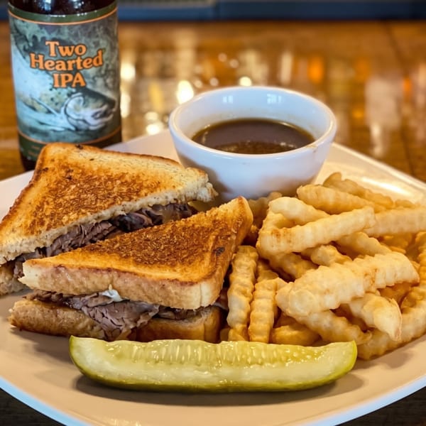 Roast beef sandwich with fries, a pickle spear, au jus, and a bottle of Two Hearted IPA.