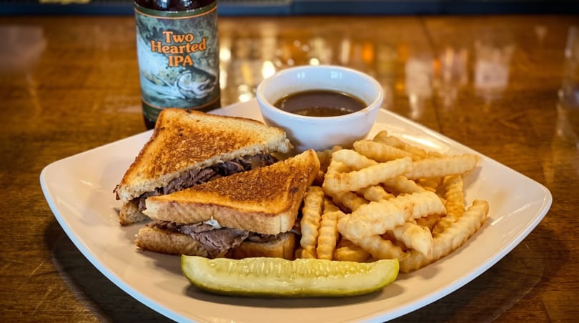 Roast beef sandwich with fries, a pickle spear, au jus, and a bottle of Two Hearted IPA.