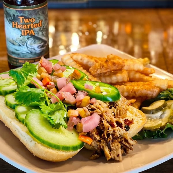 Pulled pork sandwich with cucumbers, pickled vegetables, jalapeños, fries, and a beer bottle.