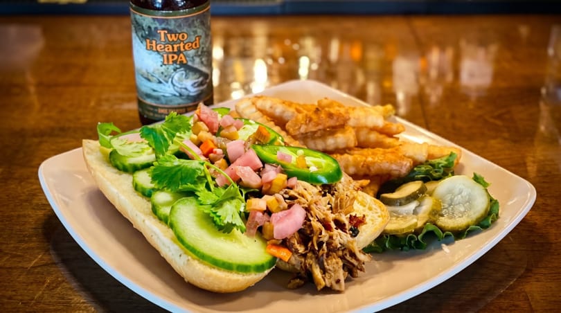 Pulled pork sandwich with cucumbers, pickled vegetables, jalapeños, fries, and a beer bottle.