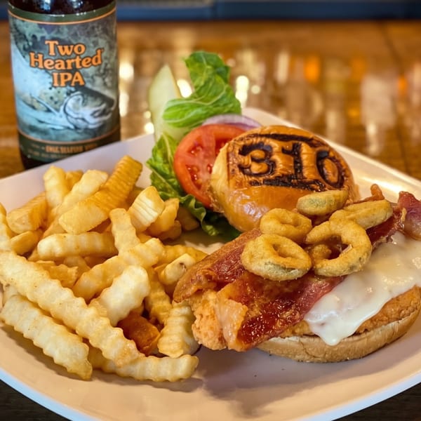 A burger with bacon, cheese, and onion rings, served with fries and a beer.