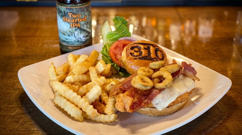 A burger with bacon, cheese, and onion rings, served with fries and a beer.