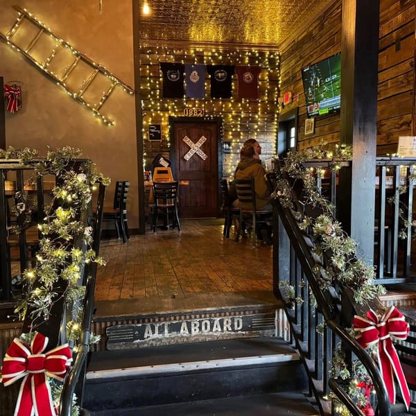Restaurant interior with festive garland, lights, and a "All Aboard" sign at the bottom of stairs.
