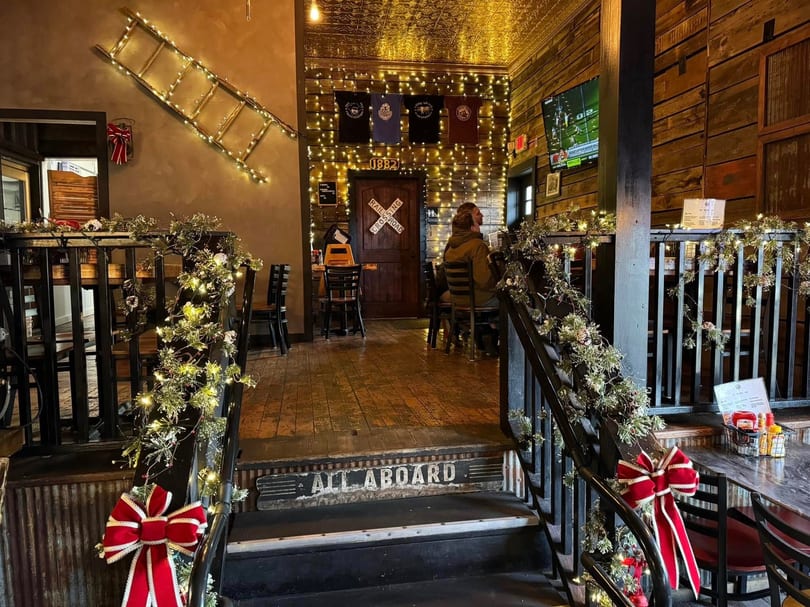 Restaurant interior with festive garland, lights, and a "All Aboard" sign at the bottom of stairs.
