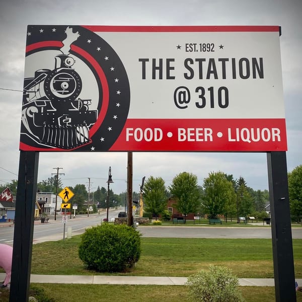 A large sign for "The Station @ 310" restaurant, featuring a train logo, food, beer, and liquor.
