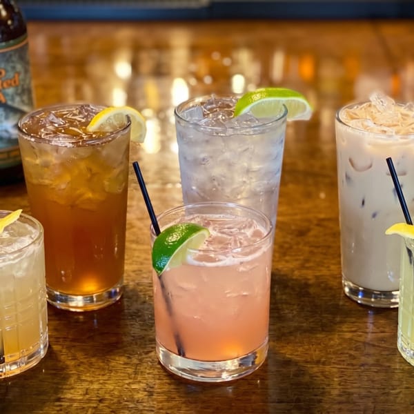 Six assorted cocktails and a bottle of Two Hearted IPA on a wooden bar.