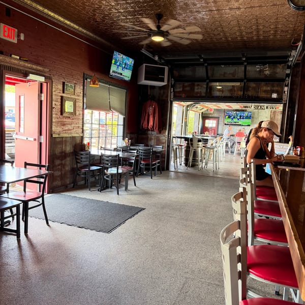 A woman sits at a bar in a rustic restaurant with a copper ceiling and open garage doors.